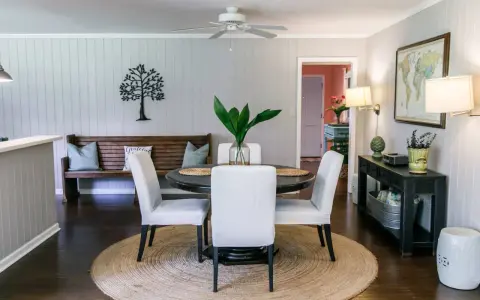 Elegante decoracion comedor pequeño con mesa redonda, sillas blancas, banco de madera y arte de árbol en la pared.