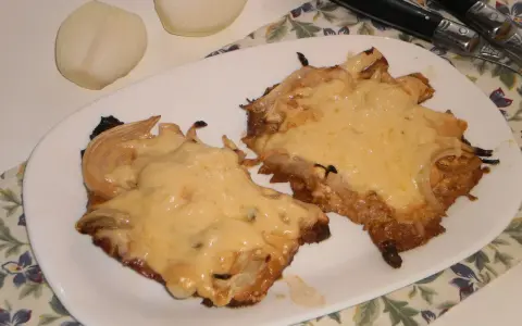 Pyszny schab w cebuli, zapieczony z serem, idealny na niedzielny obiad. Obok leżą połówki cebuli.