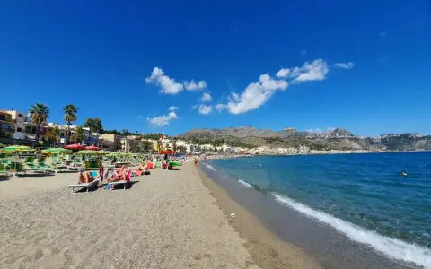 Spiaggia affollata a Giardini di Naxos, con lettini, ombrelloni e persone che si rilassano sotto il sole siciliano.