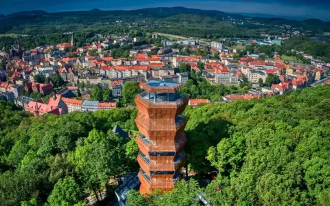 Nowoczesna wieża widokowa w otoczeniu zieleni, z panoramą miasta Wałbrzych i Sudetów Wałbrzyskich w tle.