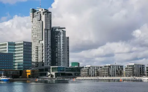 Nowoczesne budynki w Gdyni, w tym wysoki Sea Tower, nad wodą przy pochmurnym niebie.