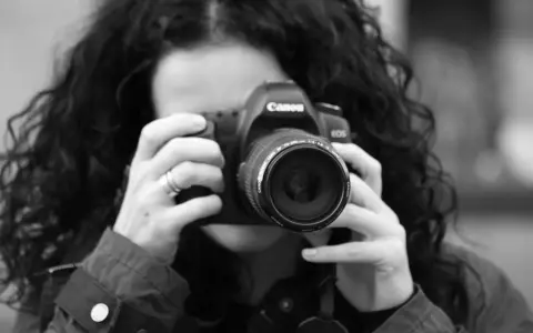Czarno-białe zdjęcie kobiety z kręconymi włosami, która trzyma aparat Canon. To jej pierwsze szkolenie z fotografii.