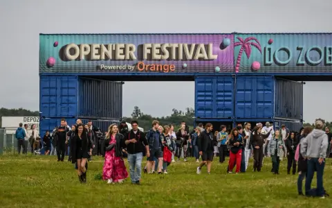 Tłum ludzi wchodzi na teren festiwalu. Nad nimi brama z napisem "OPEN'ER FESTIVAL". Kto będzie następny?