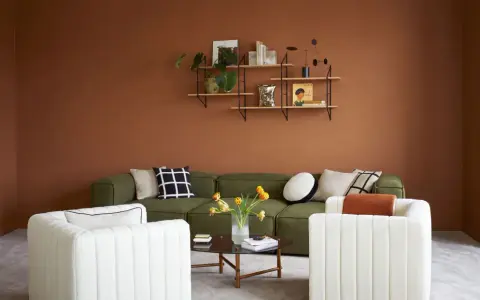 Salon cosy aux murs couleur cognac, canapé vert, fauteuils blancs et table basse.