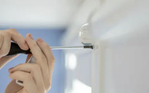 Montaż rolet okiennych z prowadnicami. Ręce przykręcają śrubę w uchwycie prowadnicy.