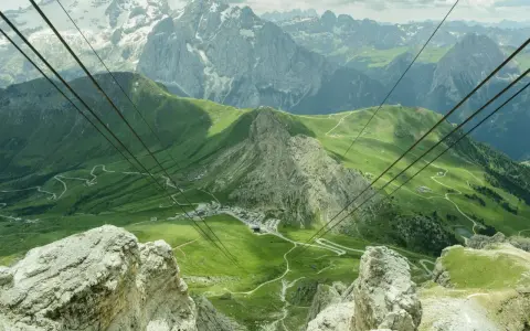 Vista mozzafiato dal passo Pordoi, con montagne innevate, verdi pendii e una strada tortuosa.