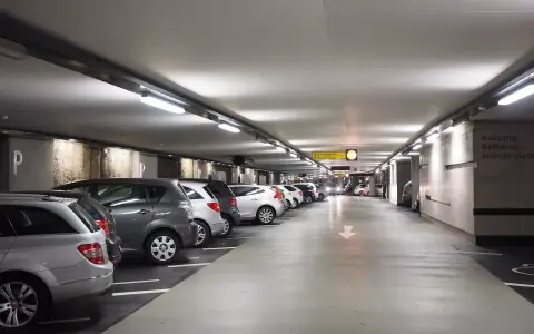 Podziemny parking z rzędami samochodów. Dostępny jest wynajem miejsca parkingowego.