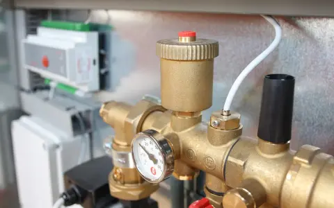 Detalle de tuberías de latón con manómetro y una válvula de seguridad. En el fondo, un panel de control.