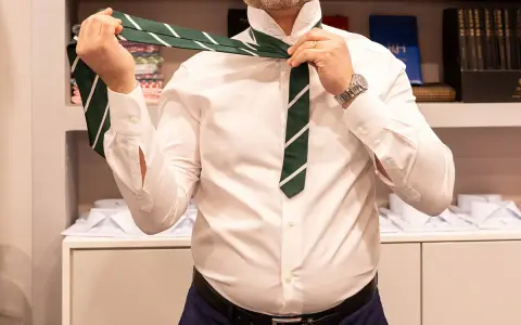 Uomo in camicia bianca che impara come fare il nodo alla cravatta verde a righe.