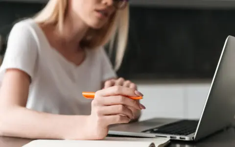 Kobieta pisze przykładowe uzasadnienie wniosku o przyznanie pomocy zdrowotnej na okulary, korzystając z laptopa i notatnika.