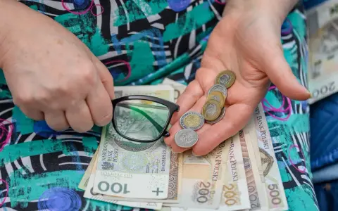 Dłonie trzymające okulary, monety i polskie banknoty.
