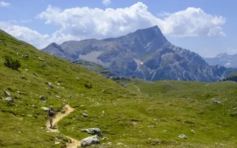 Escursionista su sentiero erboso, con imponente gruppo montuoso delle Dolomiti sullo sfondo.