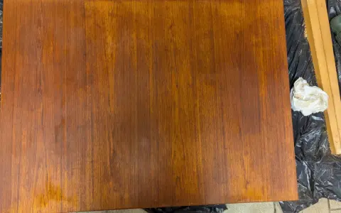 Förbereder för att slipa teakbord. En bit teak ligger på svart plast, bredvid en slipmaskin och en trasa.