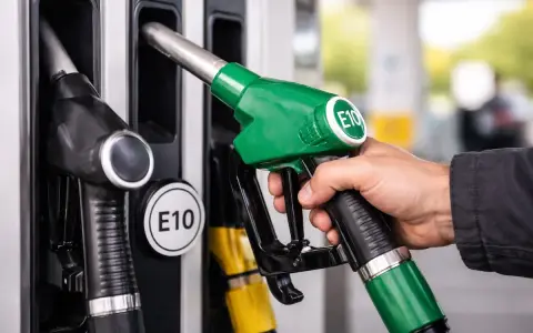 Mano che impugna una pompa di benzina verde con etichetta E10, pronta per fare rifornimento di benzina 95 ottani.