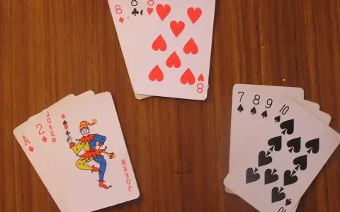 Karty na drewnianym stole: as, dwójka, joker i inne. Joker w kartach wygląda jak wesoły błazen.