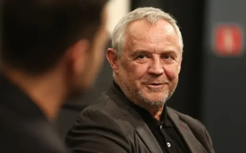 Uśmiechnięty Mikołaj Kondrat w szarym garniturze, rozmawiający z kimś niewidocznym na pierwszym planie.