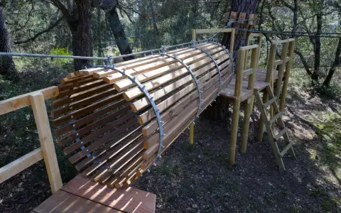 Un tunnel en bois et métal, partie d'un parcours aventure dans la forêt enchantée Venasque. Une échelle mène à une plateforme.