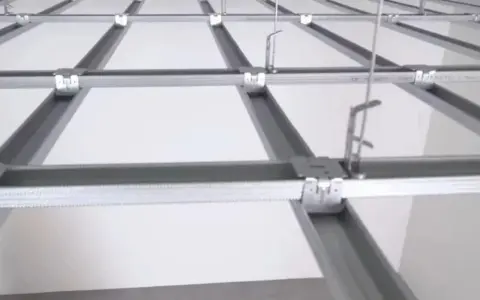 Sufit podwieszany krzyżowy z białymi panelami, tworzący siatkę. Widać elementy konstrukcji i zawieszenia.