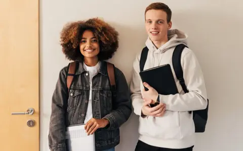 Dwóch studentów, dziewczyna z kręconymi włosami i chłopak, przygotowuje się do nauki. Może właśnie szukają informacji, jak napisać artykuł po angielsku.