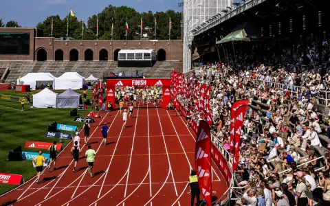 Löpare korsar mållinjen på stockholm marathon bana. Publiken jublar från läktaren.