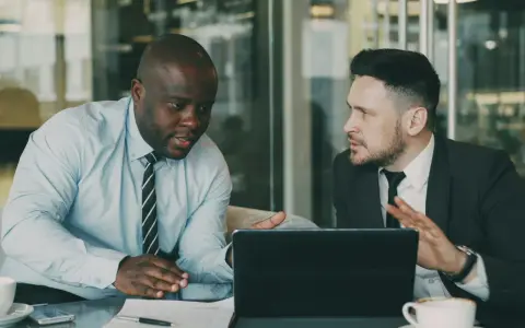 Deux hommes d'affaires discutent d'une nouvelle démarche, synonyme de succès. Ils sont concentrés sur une tablette.