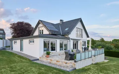 Modernes Haus mit Anbau und Terrasse. Die Solaranlage auf dem Dach deutet auf niedrige Energiekosten hin.