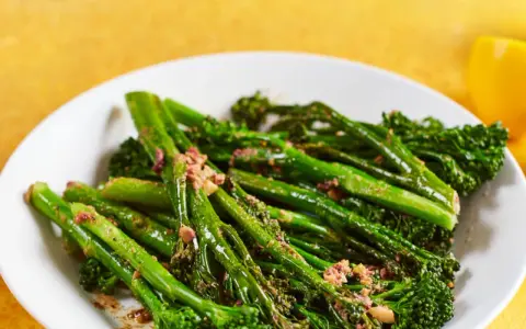 Bimi zubereiten in der Pfanne: Grüner Spargel mit knusprigen Röschen, leicht gebräunt und mit einer würzigen Kruste bestreut, auf einem weißen Teller.
