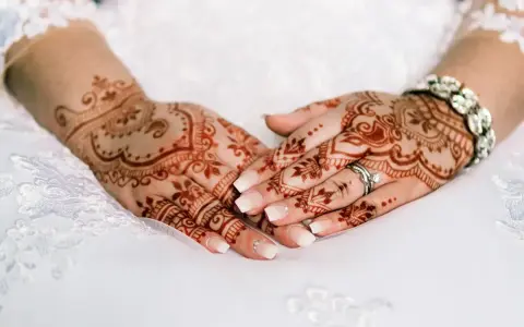 Manos de novia con intrincados diseños de henna, anillos y pulsera brillante, listas para la boda.
