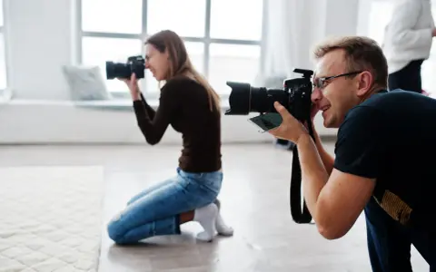 Mężczyzna i kobieta uczą się, jak zostać fotografem, ćwicząc z aparatami w studiu.