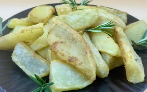 Patatas gajo doradas y crujientes, adornadas con ramitas de romero fresco, servidas en un plato oscuro.