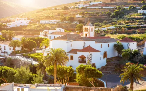 Villaggi turistici a Fuerteventura, con case bianche, palme e una chiesa con campanile, immersi nel sole dorato del tramonto.