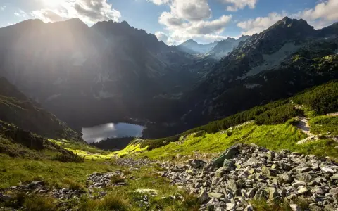 Słoneczny, skalisty krajobraz wysokogórski Tatr z jeziorem w dolinie.