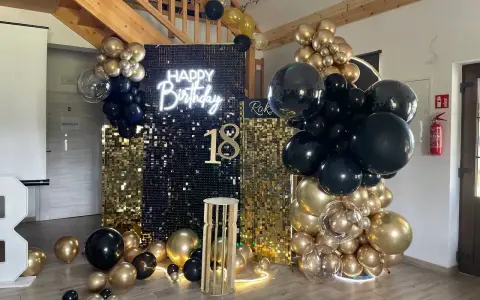 Elegancka ścianka do zdjęć na 18 urodziny z napisem "Happy Birthday" i liczbą 18, ozdobiona złotymi i czarnymi balonami.