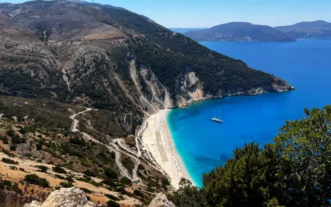 Widok na plażę Myrtos, jedno z najpiękniejszych miejsc na Kefalonii. Kręta droga prowadzi do białego piasku i turkusowej wody.