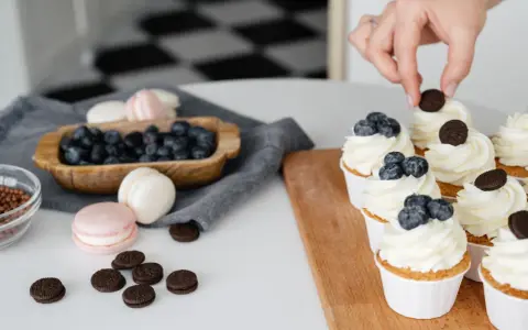 Des cupcakes décorés avec une crème chiboust aérienne, des myrtilles et des biscuits. Des macarons et des myrtilles sont disposés à côté.