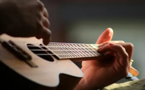 Dłonie grające na ukulele, zbliżenie na gryf i struny.