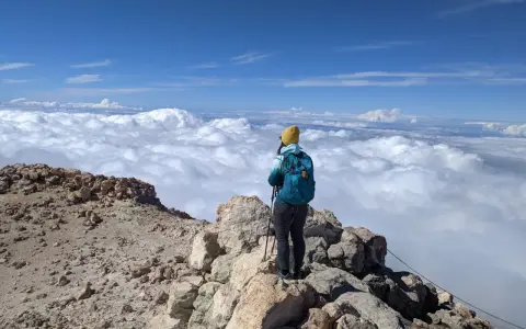 Widok z Teide: turystka w żółtej czapce podziwia morze chmur z wulkanicznego szczytu.