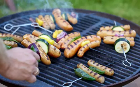 Grillad korv med grönsaker på en het grill. Röken stiger och doften sprider sig.