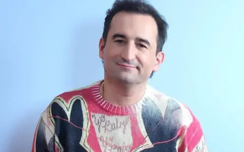 Uśmiechnięty polski aktor z autyzmem w kolorowym swetrze z sercem i napisem "Yo Baby".