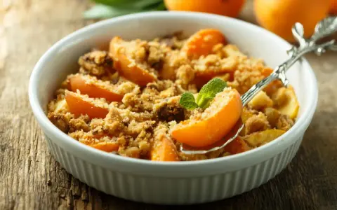 Ein köstlicher Aprikosen Crumble in einer weißen Schale, garniert mit Minze. Perfekt für einen süßen Genuss.