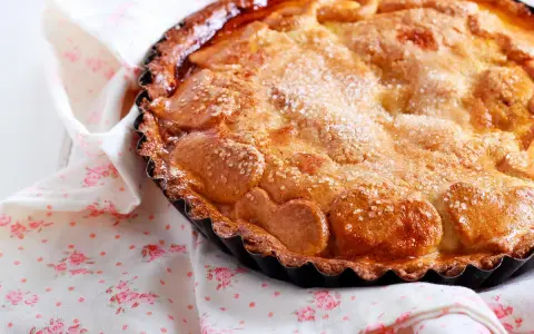 Une délicieuse tarte au sucre dorée, saupoudrée de cristaux de sucre, repose sur une serviette à motifs floraux roses.