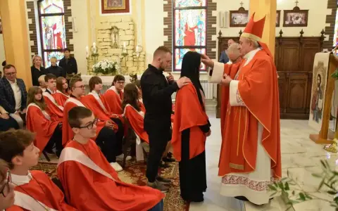 Biskup udziela sakramentu bierzmowania. Ceremonia, choć uroczysta, nie trwa długo. Młodzi ludzie w czerwonych szatach czekają na swoją kolej.