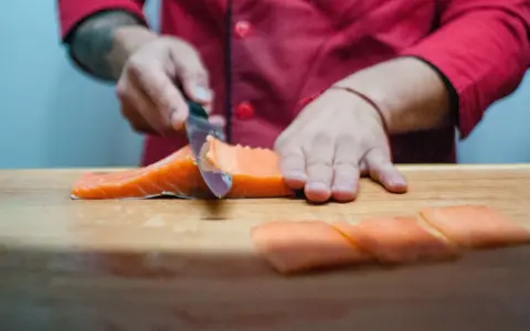 Szef kuchni kroi łososia na desce. Powstają kawałki idealne do sushi, które można zamarynować w solance.