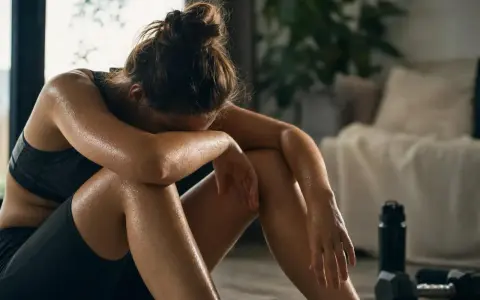 Donna esausta dopo l'allenamento, con gocce di sudore sulla pelle. Potrebbe aver bisogno di rimedi per l'overtraining.