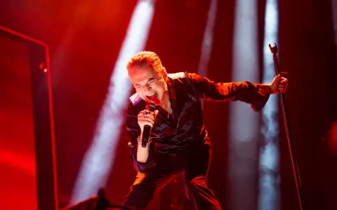 Dave Gahan sjunger passionerat under en Depeche Mode konsert, badad i rött ljus.