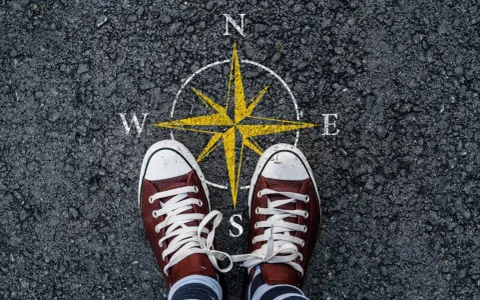 Feet stand on a compass, symbolizing the start of a journey. This image can represent the **mission creep meaning**, where initial goals expand unexpectedly.