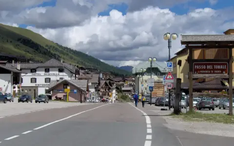 Strada verso il Passo del Tonale in moto, con case alpine e montagne sullo sfondo.