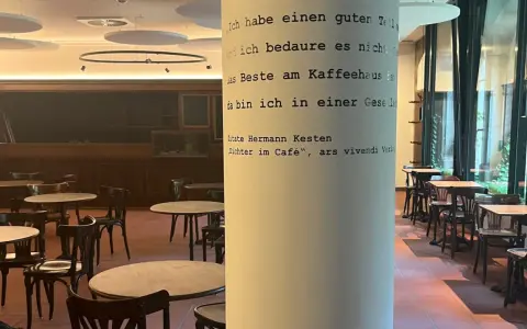 Gemütliches **cafe vegan** mit vielen Tischen und Stühlen. Eine Säule ziert ein Zitat von Hermann Kesten über das Kaffeehaus.