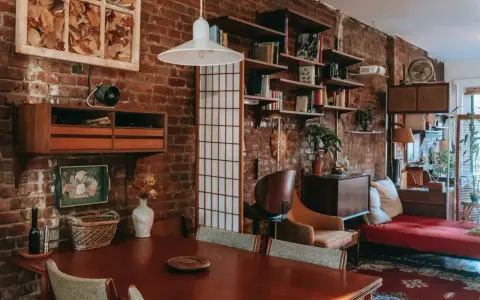 Wnętrze kawalerki z ceglaną ścianą, drewnianym stołem i meblami w stylu vintage.