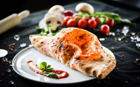 Ein goldbrauner, knuspriger Pizza Calzone mit geschmolzenem Käse und frischem Basilikum auf einem Teller.
